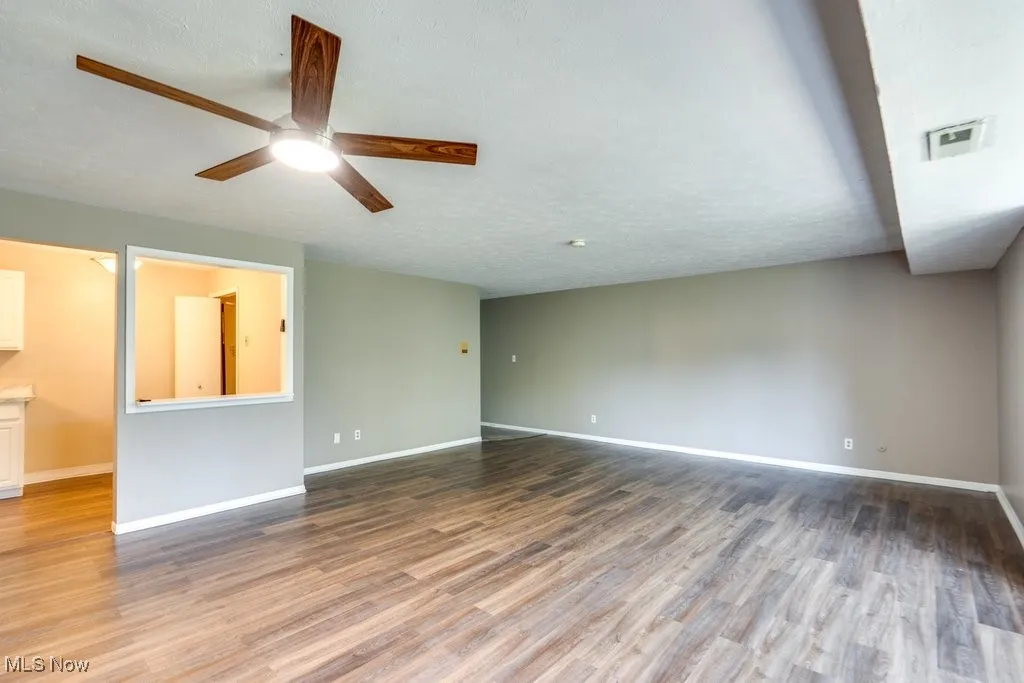 Empty room with wood finished floors, a ceiling fan, and a textured ceiling
