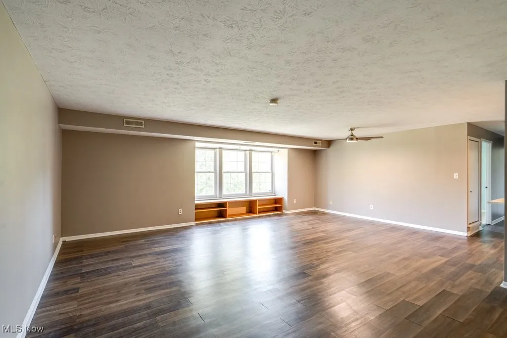 Unfurnished room with dark wood-style flooring, a textured ceiling, and ceiling fan