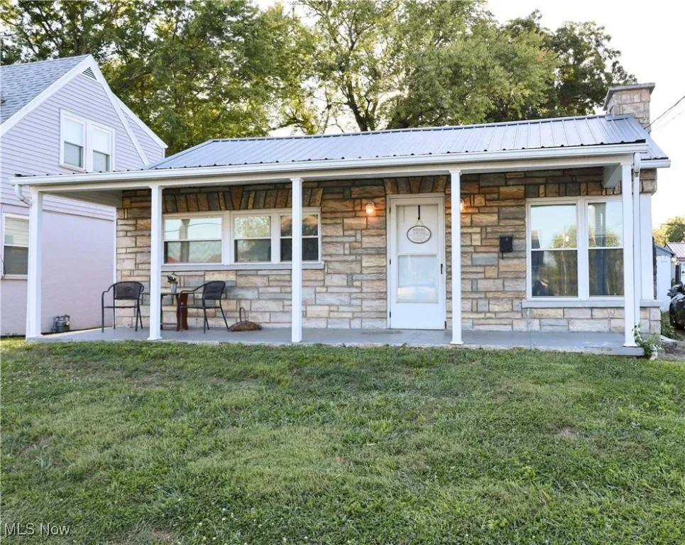 View of front of property with a porch, a front yard, stone siding, and a metal roof