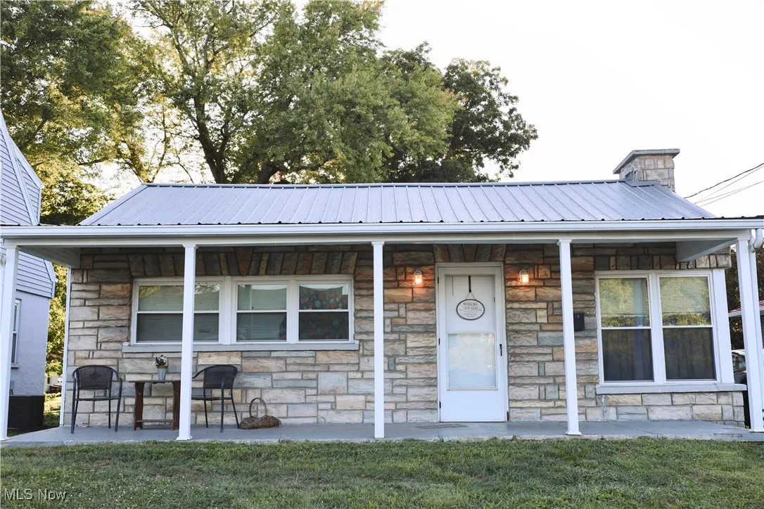 View of front of home with stone siding, a porch, and a metal roof