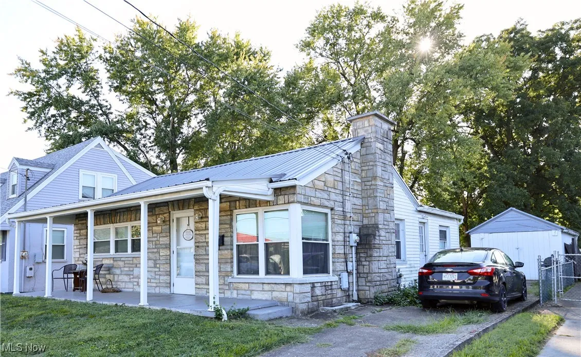 View of front facade with stone siding, covered porch, a chimney, a metal roof, and an outdoor structure