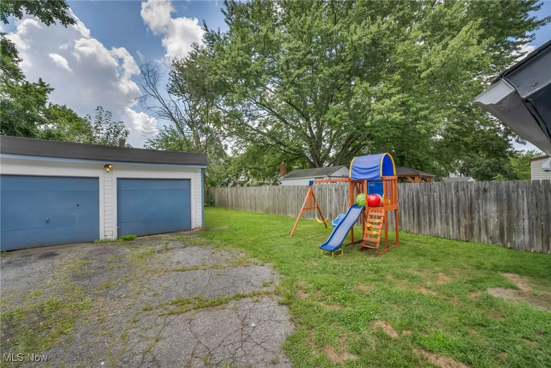 Fenced backyard with a playground, an outdoor structure, and a garage