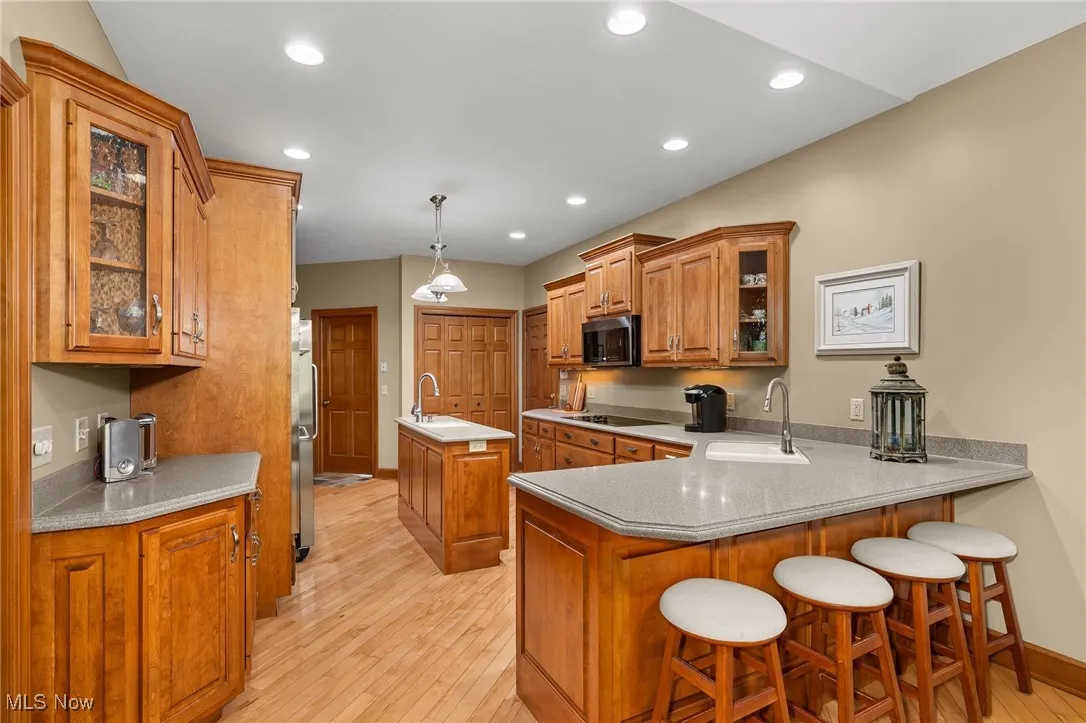 Kitchen with glass insert cabinets, brown cabinetry, a kitchen breakfast bar, a peninsula, and a kitchen island with sink