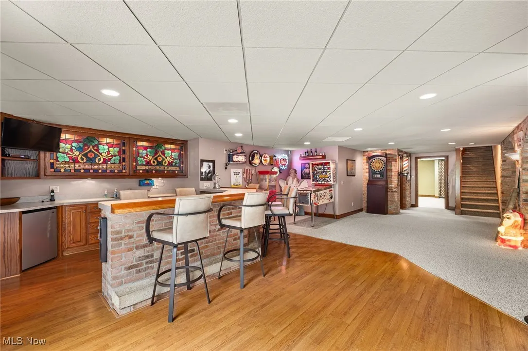 Indoor wet bar featuring brown cabinetry, stainless steel fridge, stairway, recessed lighting, and light carpet