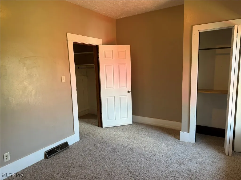 Unfurnished bedroom with a walk in closet, carpet flooring, and a textured ceiling