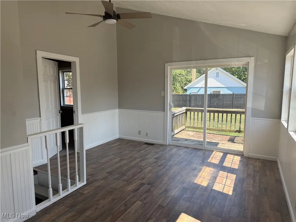 Unfurnished room with lofted ceiling, wainscoting, dark wood-style floors, and a ceiling fan