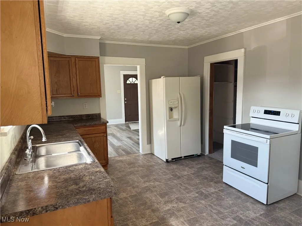 Kitchen with dark countertops, white appliances, ornamental molding, stone finish floors, and brown cabinetry