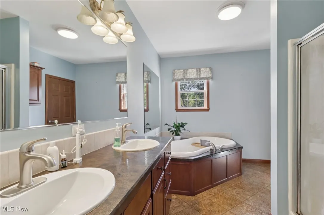 Full bathroom featuring a shower stall, double vanity, a bath, and light tile patterned floors