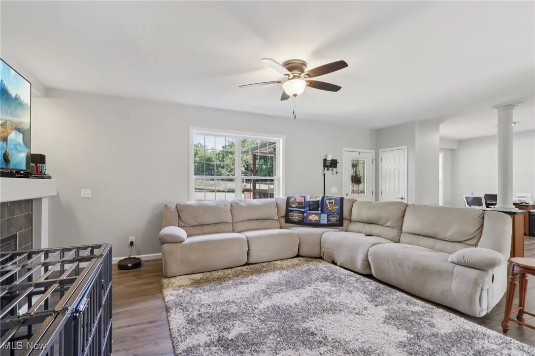 Living room featuring wood finished floors, a tile fireplace, ceiling fan, and decorative columns