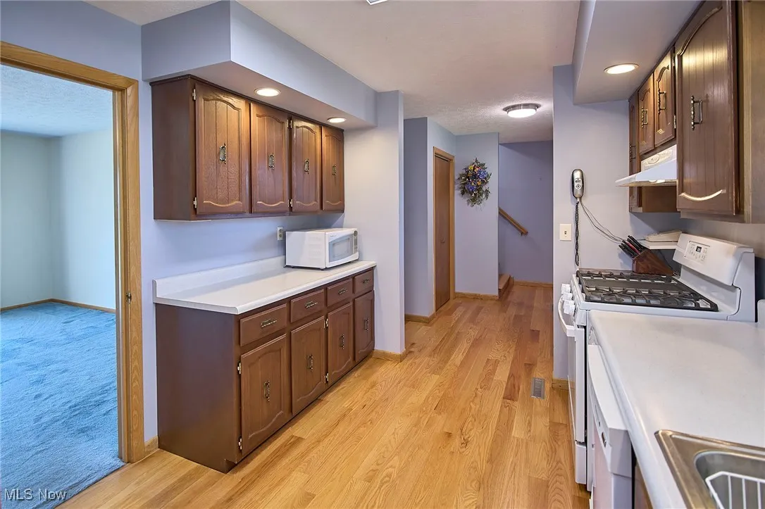 Kitchen with white appliances, light countertops, light wood-style flooring, under cabinet range hood, and recessed lighting