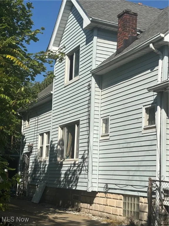 View of side of home with a shingled roof and a chimney
