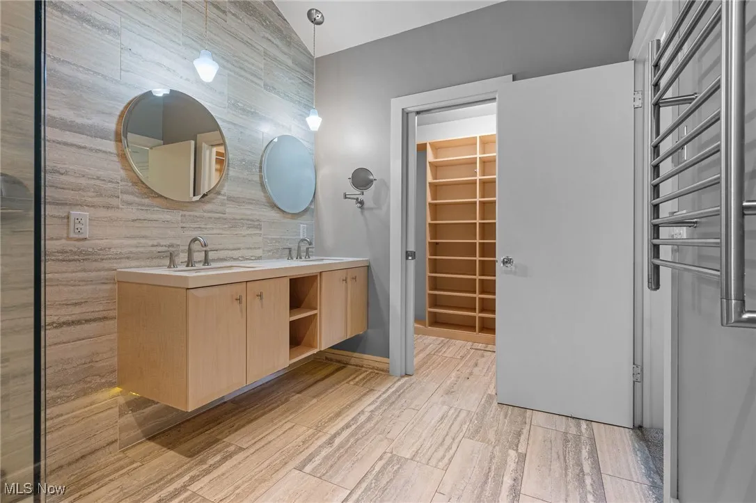 Primary bathroom with double vanity, tile walls, wood tiled floors, a towel warmer, and a walk in closet