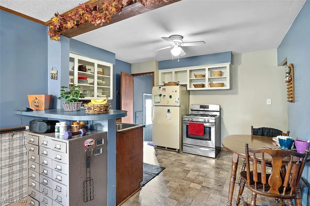 Kitchen with stainless steel gas range, freestanding refrigerator, a ceiling fan, glass insert cabinets, and dark countertops