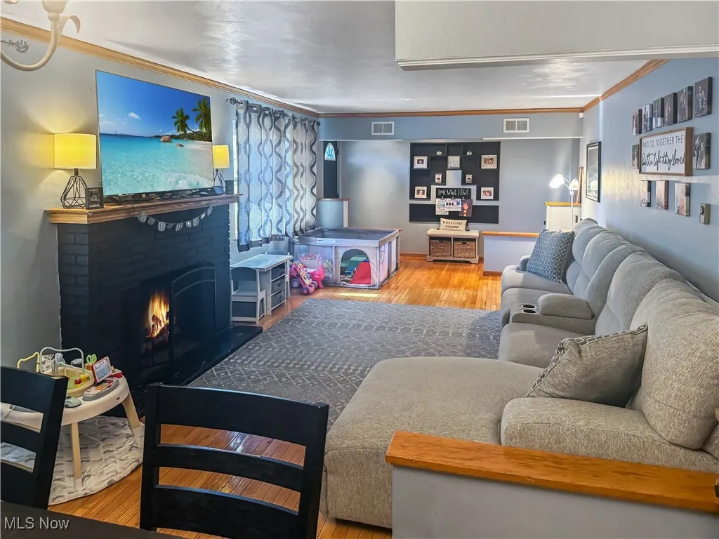Living room with ornamental molding, light wood-style floors, and a brick fireplace