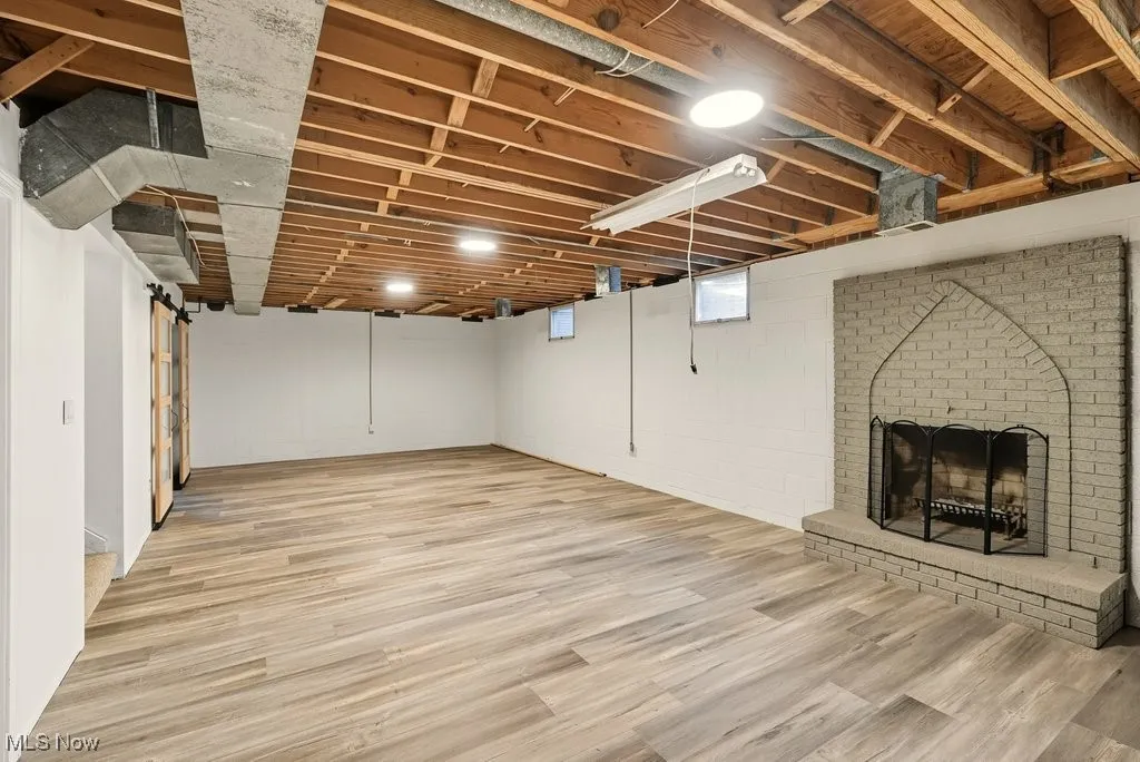 Below grade area featuring a brick fireplace, light wood finished floors, and a barn door