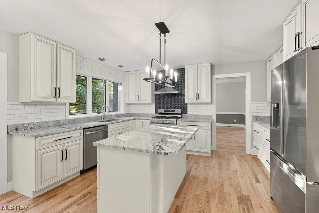 Kitchen featuring appliances with stainless steel finishes, light stone countertops, and light wood-style flooring