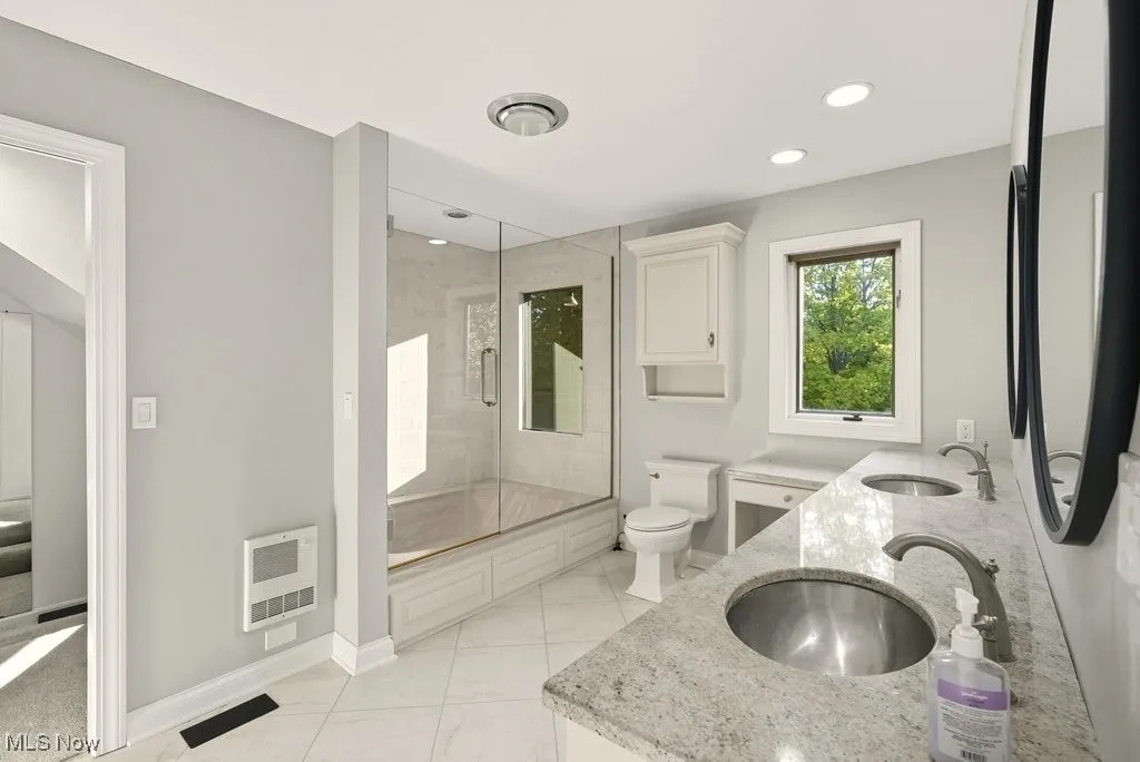 Full bathroom with double vanity, combined bath / shower with glass door, heating unit, and recessed lighting