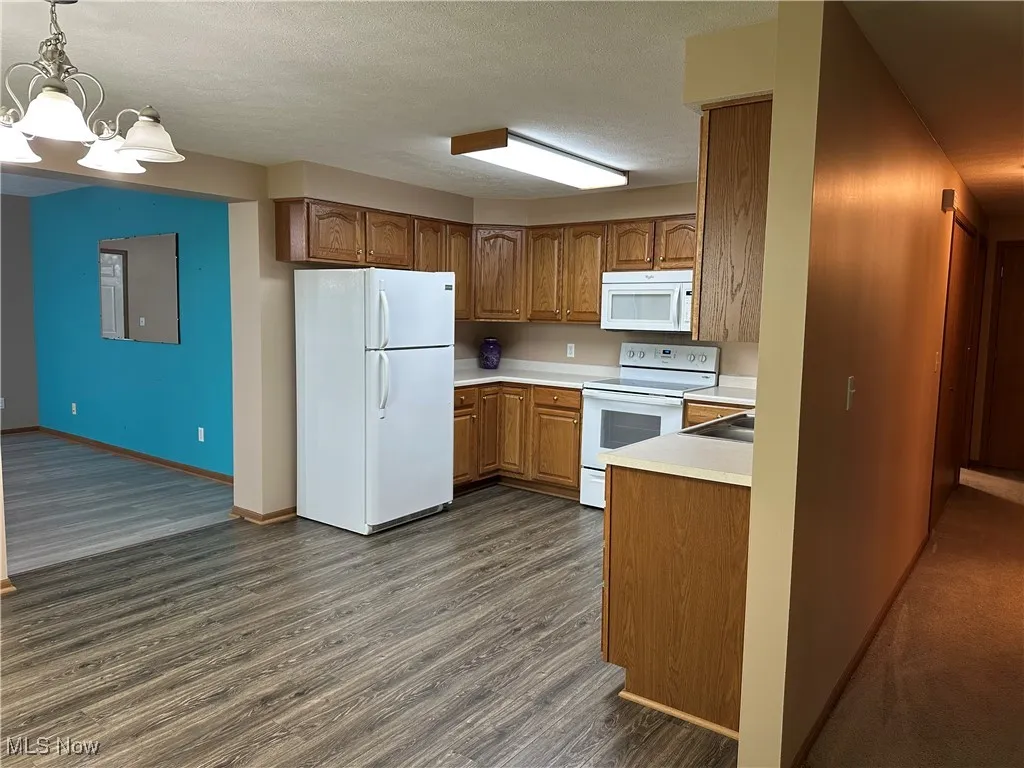 Kitchen with light countertops, white appliances, brown cabinets, dark wood-style floors, and decorative light fixtures