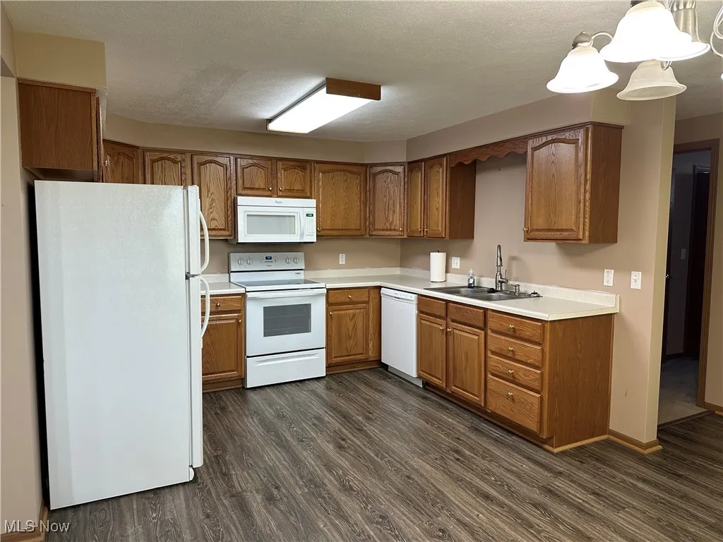Kitchen with white appliances, dark wood-style flooring, light countertops, brown cabinets, and a textured ceiling