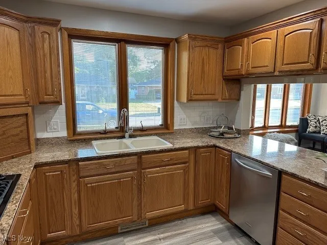Kitchen featuring healthy amount of natural light, dishwasher, brown cabinets, and dark stone countertops