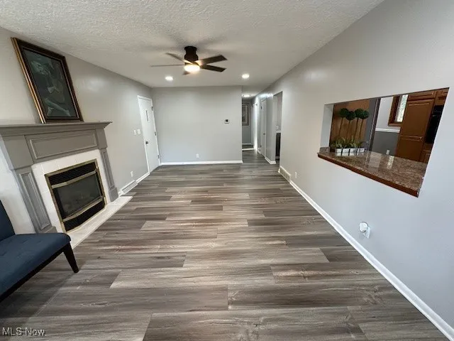Unfurnished living room featuring a textured ceiling, dark wood-type flooring, a glass covered fireplace, ceiling fan, and recessed lighting