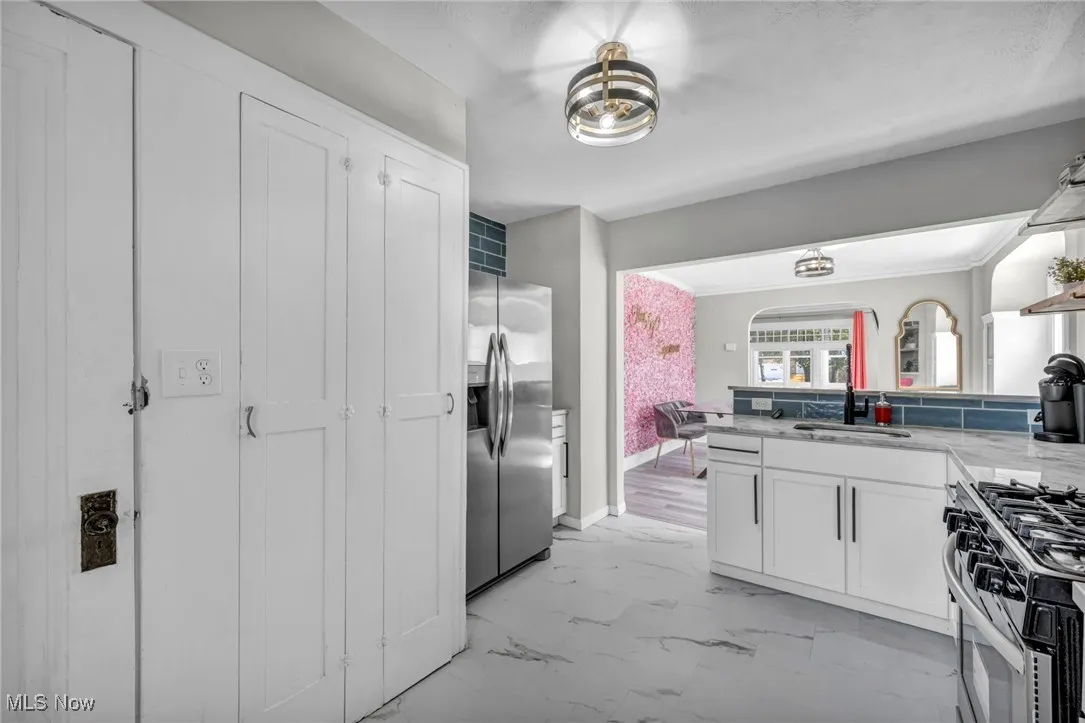 Kitchen featuring appliances with stainless steel finishes, light marble finish flooring, a peninsula, white cabinets, and light stone counters