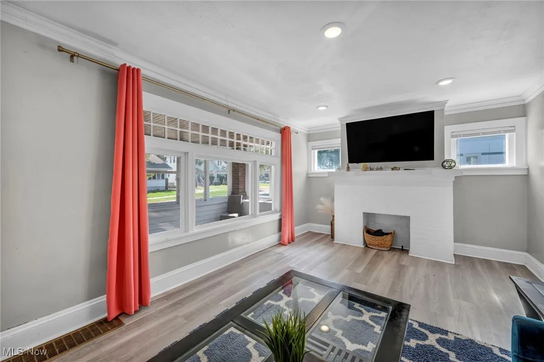 Unfurnished living room featuring ornamental molding, light wood-type flooring, a brick fireplace, and recessed lighting