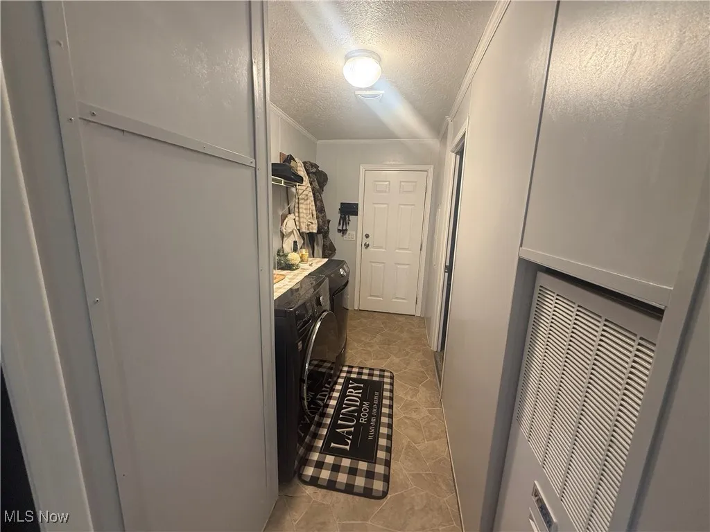 Corridor with a textured ceiling, washer and dryer, ornamental molding, and a heating unit