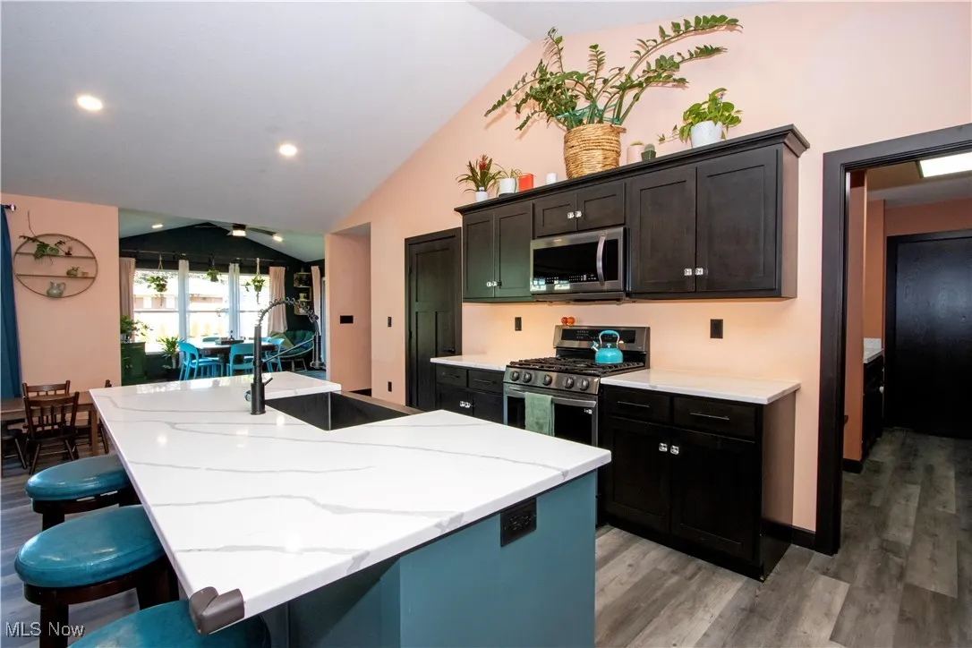 Kitchen featuring lofted ceiling, appliances with stainless steel finishes, light wood-style flooring, an island with sink, and a kitchen breakfast bar