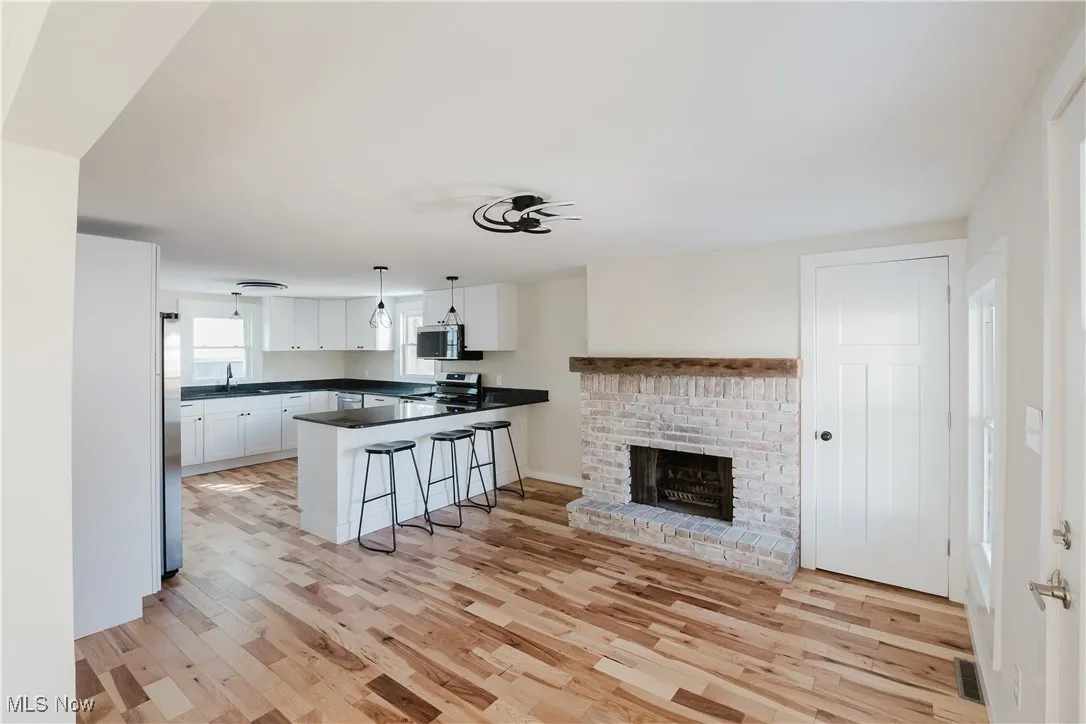 Kitchen with a breakfast bar, white cabinets, a fireplace, decorative light fixtures, and light wood-style flooring