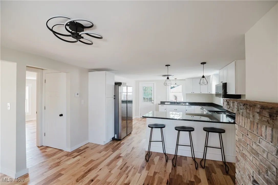 Kitchen with a peninsula, freestanding refrigerator, white cabinetry, light wood-style floors, and pendant lighting