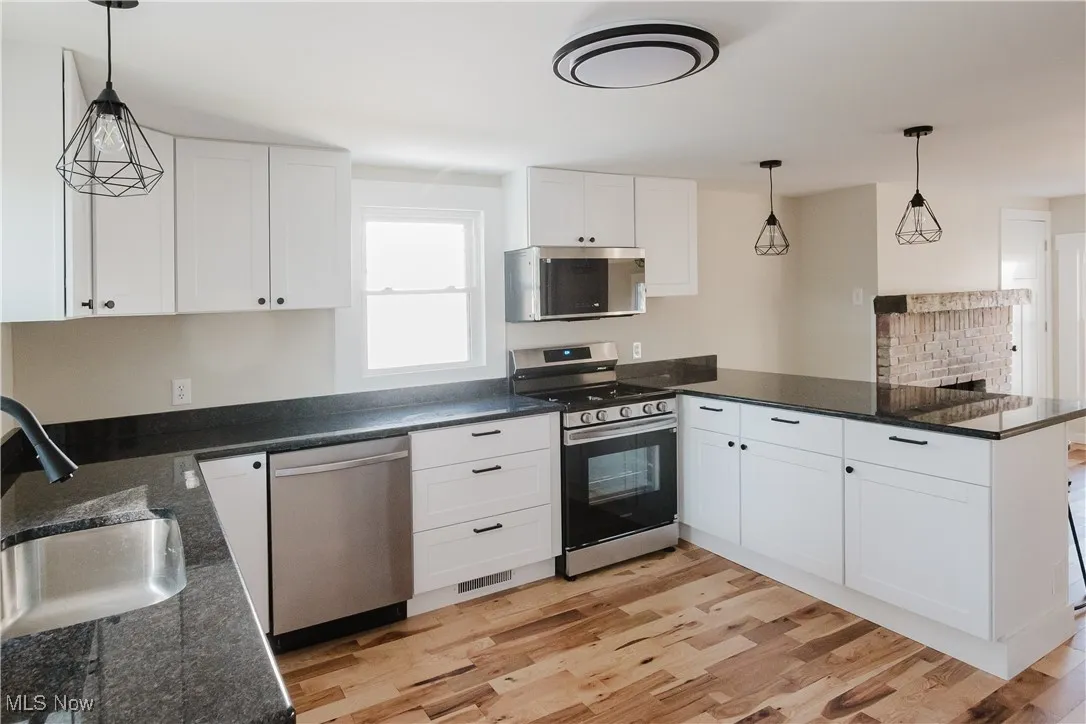 Kitchen with decorative light fixtures, a peninsula, appliances with stainless steel finishes, and light wood-style flooring