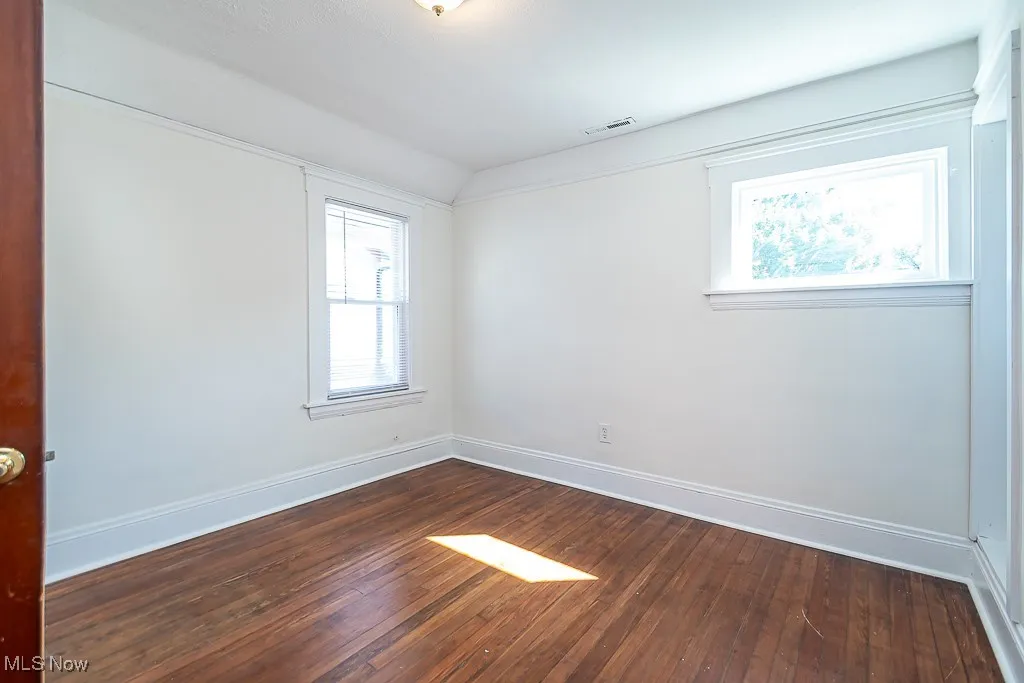 Spare room featuring dark wood-type flooring and vaulted ceiling