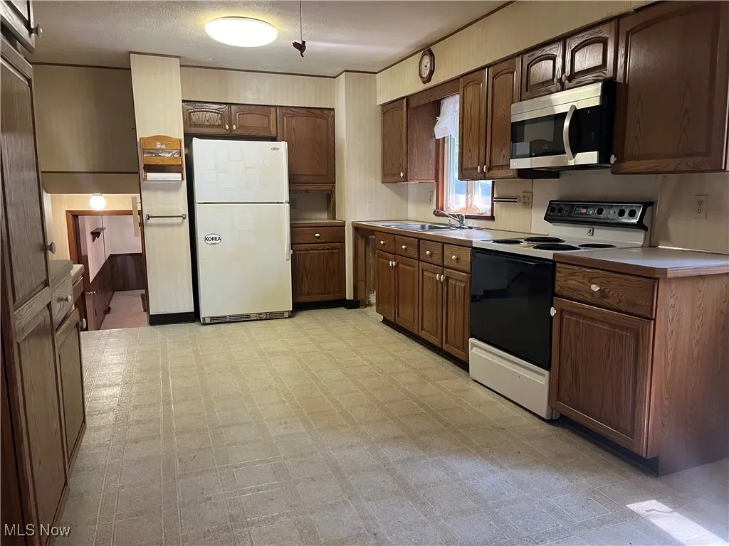 Kitchen featuring light floors, white appliances, light countertops, and dark brown cabinets