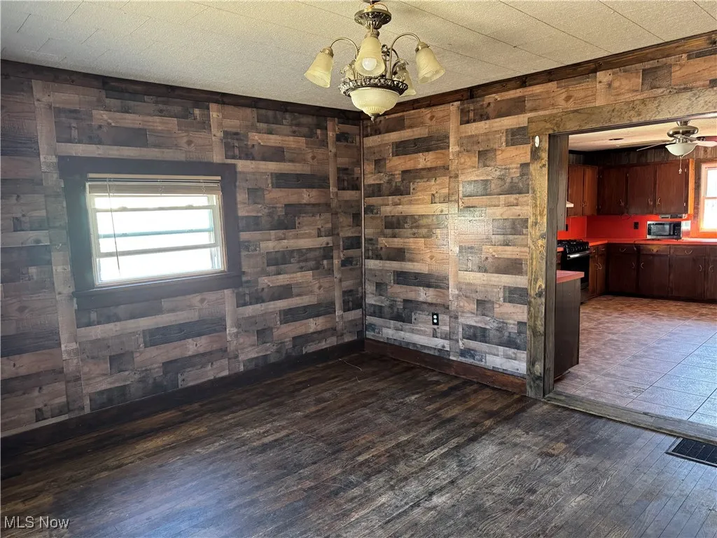 Spare room featuring wooden walls, dark wood-style floors, and a chandelier