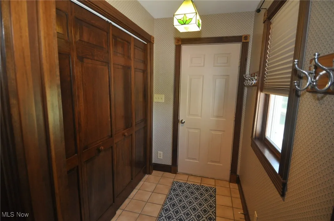 Doorway to garage with wallpapered walls and tile patterned floors, featuring laundry closet with laundry hookups