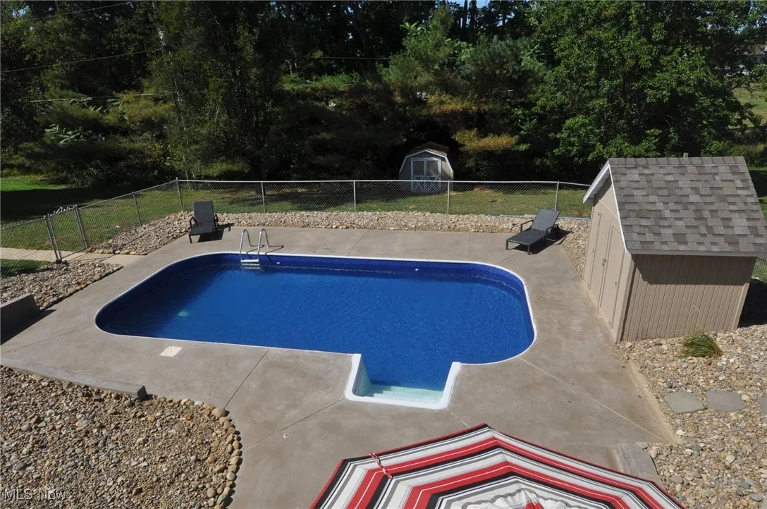 View of swimming pool with a shed, a fenced backyard, and a patio area