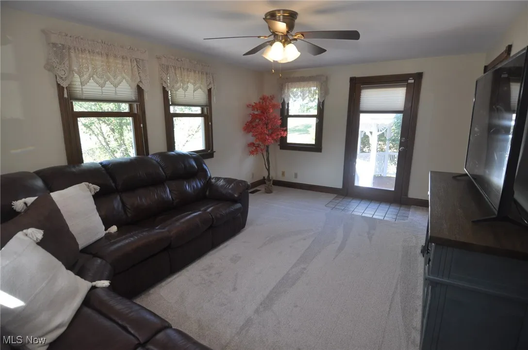 Carpeted family room featuring baseboards and a ceiling fan, door to side and rear deck down to pool area.