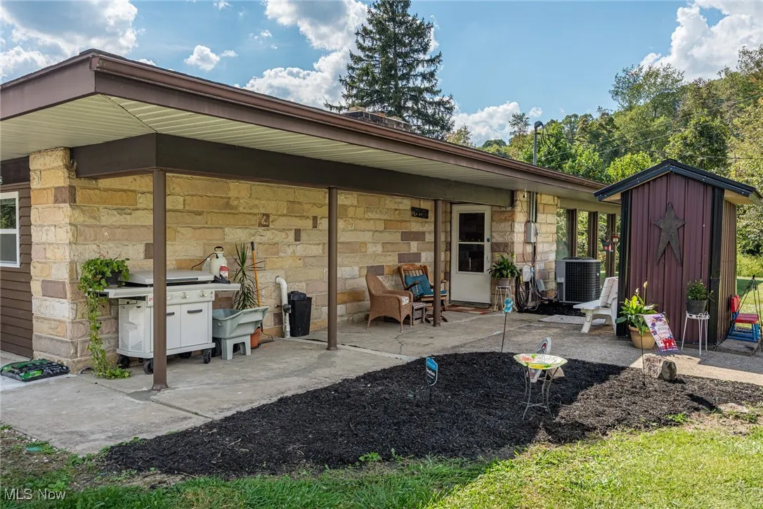 Rear view of property featuring a patio area, stone siding, and a storage shed
