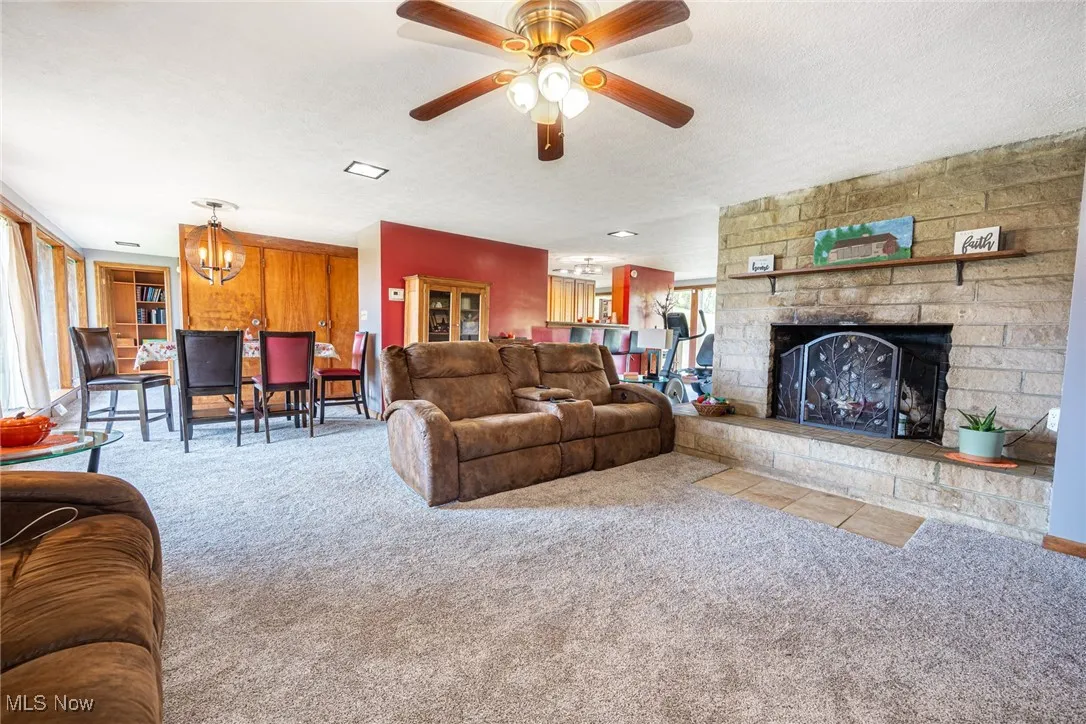 Living area featuring a chandelier, carpet, a stone fireplace, a textured ceiling, and ceiling fan