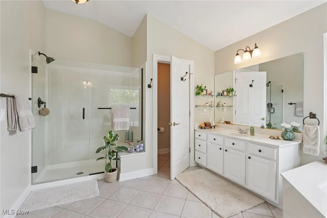 Bathroom featuring light tile patterned floors, a shower stall, vanity, lofted ceiling, and a bath