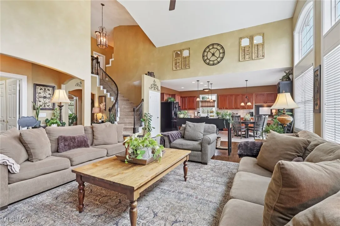 Living area with a chandelier, a high ceiling, stairs, wood finished floors, and a ceiling fan