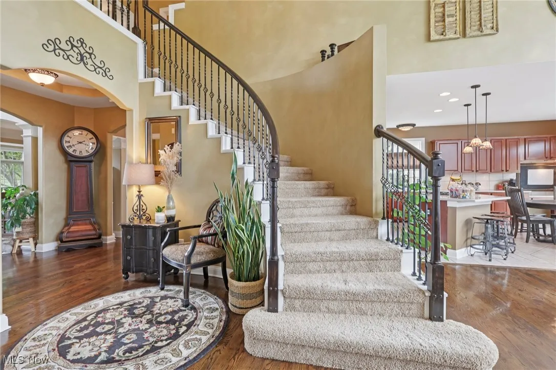 Stairs with arched walkways, wood finished floors, a towering ceiling, and recessed lighting