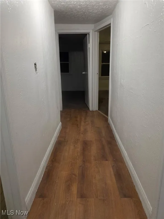 Corridor featuring a textured wall, dark wood-style flooring, and a textured ceiling