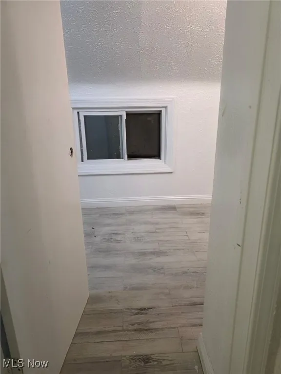 Hall with light wood-type flooring and a textured ceiling
