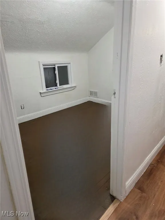 Unfurnished room with wood finished floors, a textured ceiling, and a textured wall