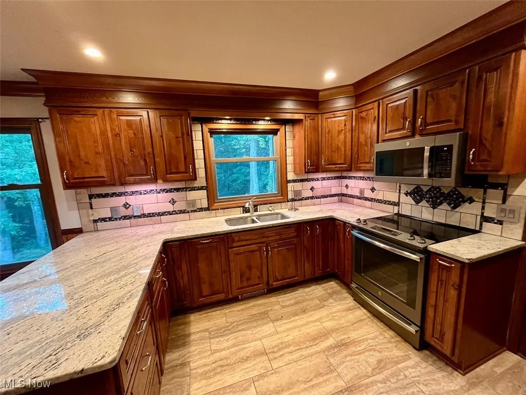Kitchen with a peninsula, appliances with stainless steel finishes, light stone countertops, backsplash, and crown molding