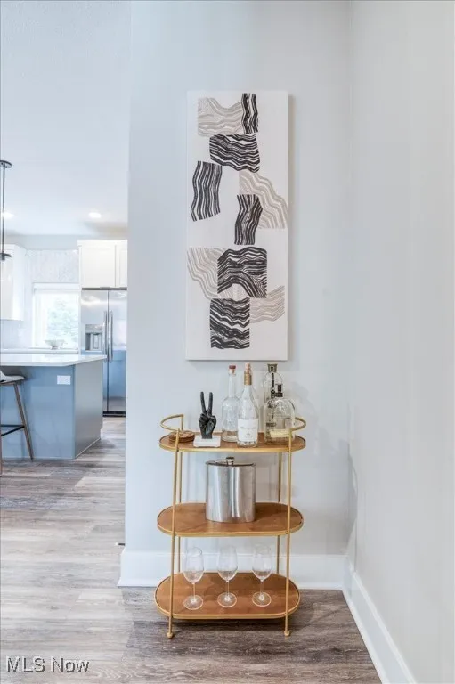 Detailed view of stainless steel refrigerator with ice dispenser, light wood finished floors, white cabinets, and a kitchen bar