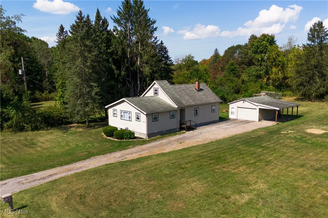 View of front of house with a front yard, an outdoor structure, driveway, a carport, and roof with shingles