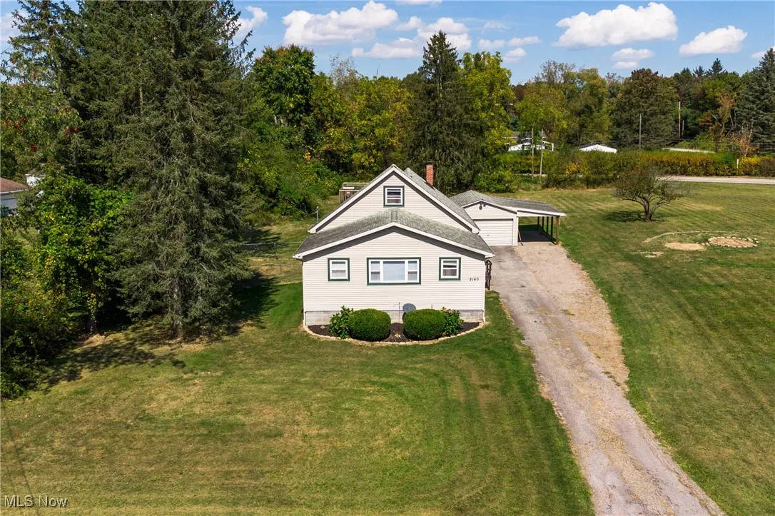 View of front facade with dirt driveway, a front lawn, a carport, a chimney, and a forest view